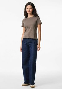 Ruskea ribattuja paita, jossa on aaltoileva helma ja hihansuut, yhdistettynä löysiin tummansinisiin farkkuihin ja beigeihin kenkiin. Yksinkertainen ja rento muotoilu.