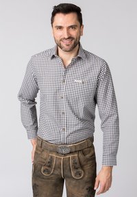 Karierte Hemd in Schwarz und Weiß, kombiniert mit braunen Lederhosen aus Leder mit floralen Prägungen und einer dekorativen Gürtelschnalle.
