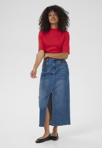 Röd kortärmad topp, kombinerad med en lång blå denimkjol med en framtass och åtsittande midja. Svarta platta skor fulländar outfiten.