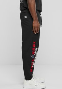 Svarte tapered joggers i bomullsblanding med rød og hvit "KANI Brooklyn" logo print, med sidelommer og elastiske mansjetter.