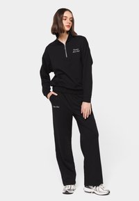 Black athletic outfit featuring a half-zip pullover with a high collar and relaxed-fit pants, both made of soft material.
