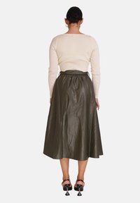 Top de manga larga color crema con textura acanalada, combinado con una falda tableada, brillante, de talle alto en verde oliva oscuro. Sandalias negras de tacón visibles.