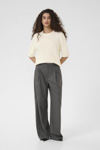 Maglione corto a maniche corte in maglia crema abbinato a pantaloni larghi grigi a vita alta, con una morbida texture e un design plissettato nella parte anteriore.
