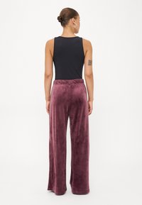 Pantaloni din catifea moale, cu talie elastică, de culoare mauve închis și croi larg, asortați cu un top negru fără mâneci. Textură netedă, croi lejer.
