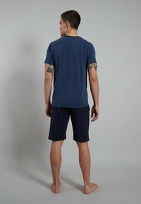 Maglietta a righe navy con maniche corte abbinata a pantaloni corti navy. Il tessuto sembra morbido e con una vestibilità rilassata, adatta per un abbigliamento casual.