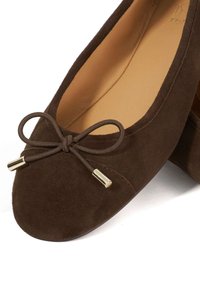 Bruine suède ballerina's met een ronde neus en een decoratieve strik met gouden hardware accenten. Glad interieurvoering.