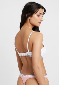 Witte bh met verstelbare bandjes en haaksluiting, gecombineerd met een roze en witte gestreepte string met een merkband.