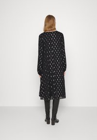 Robe noire à manches longues, avec un délicat motif de feuilles blanches, longueur mi-mollet et tissu léger. Associée à des bottes noires montantes.
