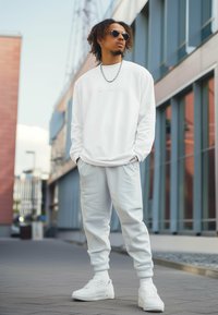 Felpa bianca a maniche lunghe e pantaloni jogger coordinati, con un logo discreto. Abbinati a sneaker bianche e occhiali da sole rotondi. Tessuto liscio.