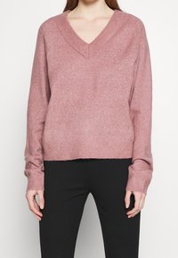 V-ringad rosa tröja i mjukt, stickat material med ribbade manschetter och nederkant, med en avslappnad passform som slutar vid midjan.