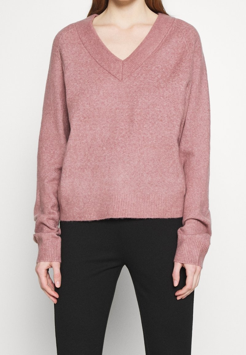 V-ringad rosa tröja i mjukt, stickat material med ribbade manschetter och nederkant, med en avslappnad passform som slutar vid midjan.