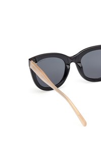 Černé sluneční brýle ve tvaru kočičích očí s tmavými skly. Průhledné, světlé stranice. Hladký plastový rám s lesklým povrchem.