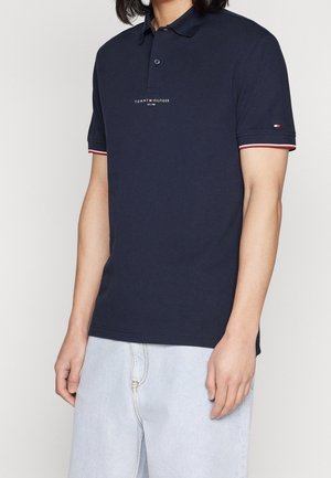Marineblaues Poloshirt aus Baumwolle, mit einem Kragen-Design, einem Logo auf der Brust und kontrastierenden roten und weißen Akzenten an den Ärmeln.