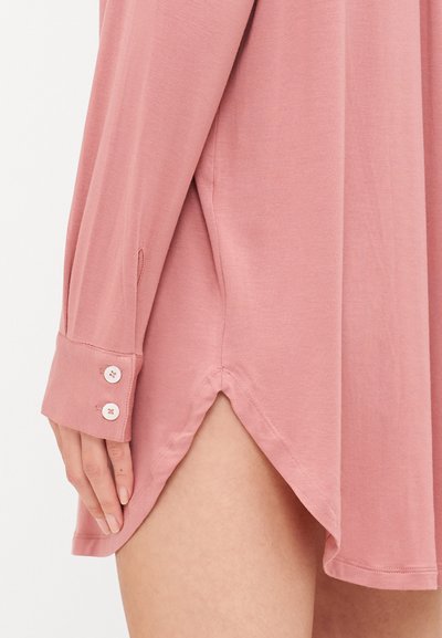 Ροζ μπλουζάκι με μακριά μανίκια, μαλακό ύφασμα, λεπτομέρεια με πλαϊνές σχισμές, κουμπωτός καρπός με τρία κουμπιά, λεία υφή, χαλαρή εφαρμογή.