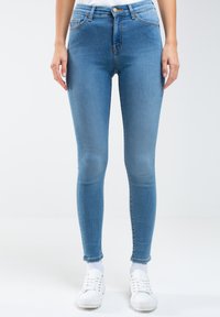 Jeans ajustados de mezclilla azul claro, con cintura alta, bolsillos frontales y una textura suave. Combinados con zapatillas blancas.
