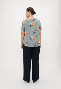 Blus med blommönster i ljusblått, kort ärm, nyckelhålsdetalj på baksidan. Kombinerad med svarta vida byxor för en avslappnad passform.