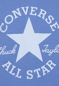 T-shirt azzurro chiaro con un design a stella bianca e testo "CONVERSE" e "ALL STAR" in lettere grasse e arrotondate. Texture morbida in cotone.