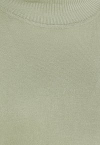 Pull en maille côtelée vert clair avec un col rond et une texture fine. Le tissu semble doux et léger, présentant un motif uniforme.