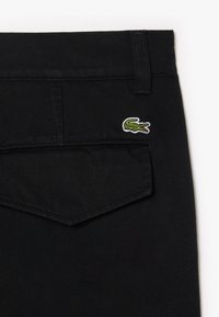 Zwarte broek van duurzaam materiaal met een chevron-ontwerp voor de zakken. Opvallende borduring van een groen en wit krokodil logo.