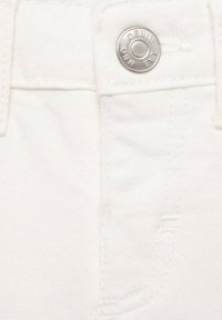 Prim-plan cu țesătură de denim alb, evidențiind un buton metalic cu inscripția "DENIM", alături de detalii de cusături și o mică buzunar frontal.
