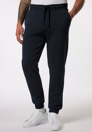 Marineblauwe trainingsbroek van zachte stof, met een elastische tailleband met koord, zijzakken en taps toelopende boorden, gedragen met witte sneakers.