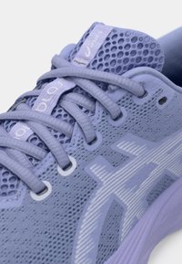 Ανοιχτό μωβ αθλητικό παπούτσι με πλέγμα στην πάνω επιφάνεια, υφασμάτινη υφή, επενδεδυμένη γλώσσα και αντίθετες λευκές λεπτομέρειες και λογότυπα. Τα κορδόνια είναι επίπεδα και γκρι.