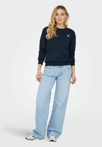 Sweatshirt marine en coton avec un col rond, des poignets côtelés et un petit logo d'ours sur la poitrine, associé à un jean clair à jambes larges.