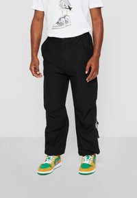 Pantalones cargo negros con bolsillos laterales, combinados con una camiseta blanca con un estampado gráfico. Zapatillas de colores con acentos en verde, naranja y blanco.