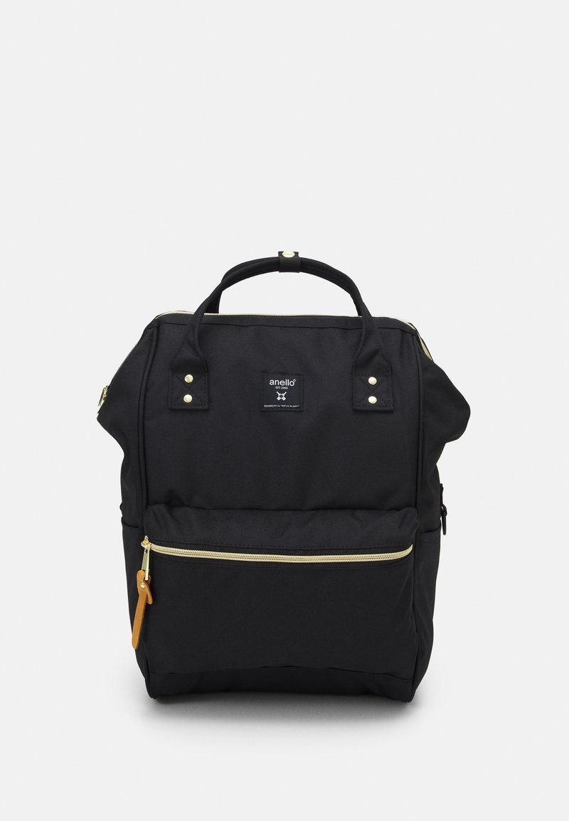 Sac à dos en tissu noir avec accents dorés et fermeture éclair, deux poignées supérieures, poche avant et un design robuste. Dispose d'un patch logo à l'avant.