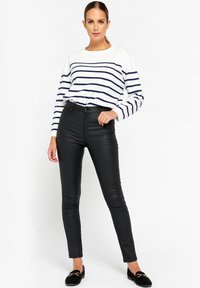 Čierne legíny z faux kože v kombinácii s bielym a námorníckym pruhovaným sveterom. Legíny sú úzke, s vysokým pásom a minimálnym hardvérom.