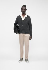 Tumehall, soonikkoelise mustriga kardigan v-kaelusega ja nööpidega, beežis stiilsed püksid ja hallid tossud. Hoides musta kotti. Lihtne disain.