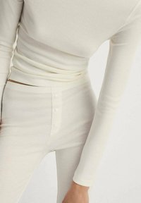 Bluză lungă cu mâneci, din material cu striații, de culoare crem, cu un design ajustat și guler înalt, combinată cu pantaloni asortați cu talie înaltă și un nasture în față.