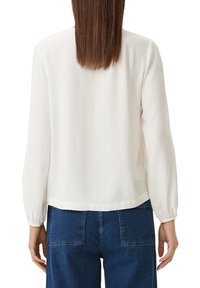 White long-sleeve blouse with a smooth texture, rounded hem, and elastic cuffs, paired with dark blue high-waisted jeans.