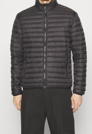 Czarna pikowana kurtka puchowa z przednim zamkiem błyskawicznym i zamykanymi na zamek kieszeniami po bokach, noszona z czarnymi spodniami.