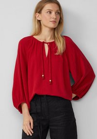 Rote locker sitzende Bluse aus strukturiertem Stoff, mit rundem Ausschnitt und Schlüsselloch-Detail, versehen mit Kordeln und Holzperlenakzenten.