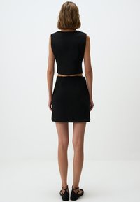 Schwarzes ärmelloses Crop-Top, kombiniert mit einem passenden schwarzen Rock. Glatte Stoffe, figurbetontes Design, minimalistische Nähte und gerade Saumlinie. Schlichte Schuhe.
