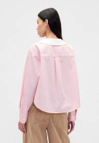 Roze-wit gestreept shirt met een ronde witte kraag, lange mouwen en een gebogen zoom, gemaakt van lichtgewicht stof.