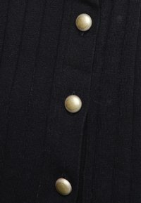 Czarna prążkowana tkanina z czterema dużymi guzikami w kolorze złotym. Tekstura wydaje się miękka i lekko elastyczna. Guziki mają dekoracyjny brzeg.