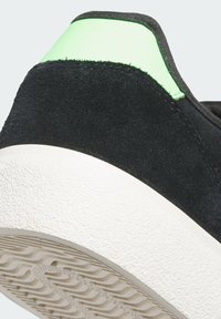 Černé semišové tenisky s podpatkem a texturovanou bílou gumovou podrážkou, na vrchním okraji s jasně zeleným akcentem.