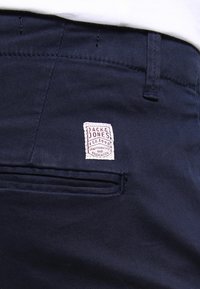 Námorně modré kalhoty z bavlněné směsi s hladkou texturou. Obsahují nášivku s logem "Jack & Jones" a detail zadní kapsy.