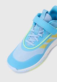 Chaussure de sport bleu clair en matériaux synthétiques et en mesh, avec des accents jaunes et une sangle Velcro sur les lacets pour un maintien sécurisé.