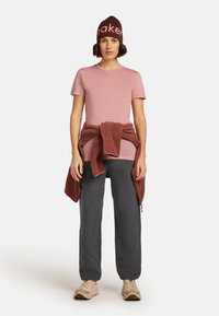 Camiseta rosa de manga corta, suéter marrón atado a la cintura, pantalones de chándal grises y zapatillas beige. Gorro marrón con detalle de texto.