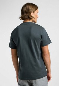 Maglietta in cotone grigio scuro con collo tondo e maniche corte. Il retro presenta una texture semplice e liscia senza motivi o loghi visibili.