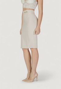 Falda lápiz de talle alto color beige con dos botones dorados, textura suave, hasta la rodilla, combinada con tacones nude.