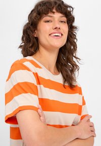 Gestreiftes Jersey-T-Shirt mit orangefarbenen und beigen horizontalen Streifen, kurzen Ärmeln, rundem Halsausschnitt und weicher, glatter Textur.