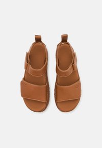 Sandales en cuir marron avec bout fermé, bride en Velcro, semelle intérieure texturée et coutures contrastées. Logo visible sur une des brides.