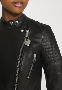 Svart lädermotorcykeljacka med kviltade axelinsatser, asymmetrisk dragkedja och detalj i silver med varumärkeslogotyp. Klassisk krage.