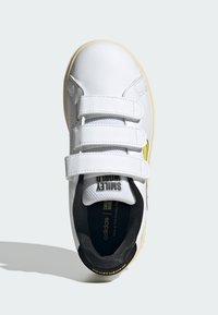 Bijela tenisica s čičak trakama, gumeni đon, crni unutarnji oblog i žuti detalj. Gornji dio od glatke kože s perforiranim detaljima.