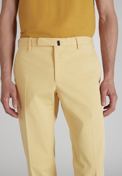 Jasnożółte, dopasowane spodnie z bawełny o gładkiej teksturze; posiadają zapięcie z przodu i kieszenie boczne.
