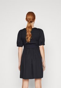 Svart klänning med en smockad bodice, puffärmar och en utsvängd kjol. Slät textur med en enkel design, sedd bakifrån.